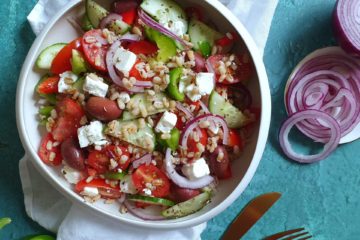 photo culinaire d'une salade grecque avec de l'orge monde, assiette colorée sur un fond turquoise