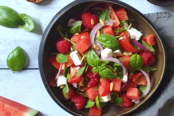 photo culinaire d'une salade de tomates, pastèque et feta, agrémentée de framboises, menthe, basilic et pignons de pin. Une assiette colorée et estivale