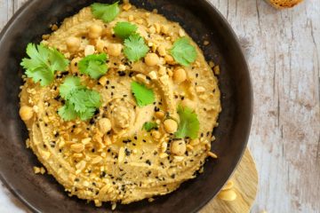 photo culinaire d'un houmous aux cacahuètes caramélisées avec des graines de sésame, de l'huile d'olive, du citron vert et de la coriandre