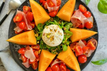 photo culinaire d'une assiette estivale avec du melon, du jambon cru, des tomates, une burrata et des pistaches concassées
