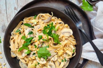 photo culinaire d'un plat de pâtes crémeuses à l'ail rôti et champignons avec du persil et des pignons de pin dans une ambiance forestière