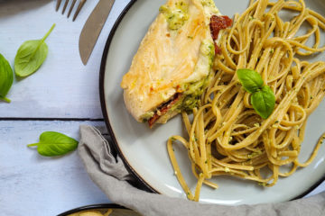 photo culinaire d'un poulet au pesto, mozzarella et tomates séchées avec des pâtes au pesto et quelques feuilles de basilic