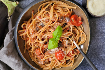 photo culinaire d'un plat de pâtes avec de la bolognaise veggie aux aubergines servi avec du parmesan râpé et du basilic