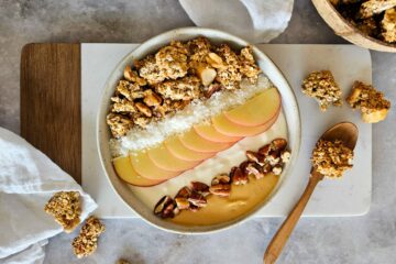 photo culinaire d'un banana granola à la cacahuète avec des grosses pépites de granola, des oléagineux et servi dans un bowl avec du yaourt, des tranches de pommes, des noix et de la purée de cacahuètes