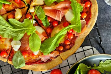 photo culinaire d'une pizza IG bas mozzarella et proscuitto avec de la roquette et des petites tomates cerise