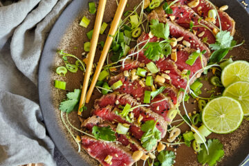 photo culinaire d'un tataki de bœuf sauce ponzu avec des cébettes, de la coriandre, des cacahuètes et des jeunes pousses