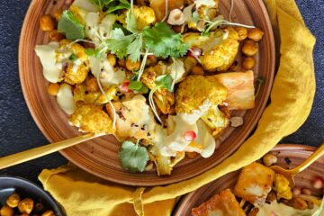 photo culinaire de chou-fleur rôtI aux épices, halloumi et sauce au curcuma et servis avec des graines de grenade, des morceaux de noisettes, de la coriandre et des pois chiches