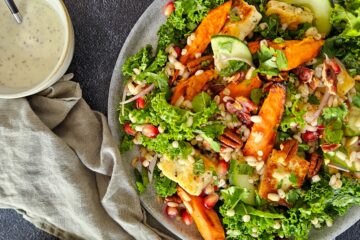 photo culinaire d'une salade d'orge, carottes rôties et chou kale avec des noix de pécan caramélisées, des graines de grenade, du concombre et du halloumi et une sauce au sumac