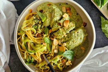 photo culinaire d'un poulet au pesto crémeux à base de basilic et de noix de cajou servi avec des pâtes complètes, des spaghettis de courgettes et des amandes effilées