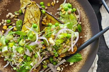 photo culinaire d'une aubergine et crème de petits pois avec de la feta, de la menthe, des oignons rouge et des pistaches