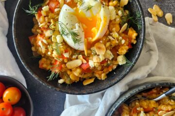 photo culinaire d'un risotto d'orge aux légumes caramélisés et feta avec un oeuf mollet et des amandes effilées, avec des poivrons et des tomates cerise