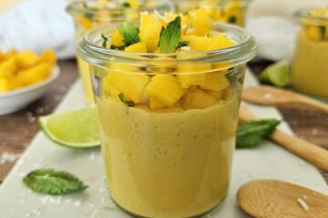 photo culinaire d'une panna cotta à la mangue, coco et citron vert avec des morceaux de mangue et de la menthe par dessus