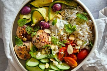 photo culinaire d'un bowl méditerranéen aux boulettes de poulet à la grecque avec des tomates cerise, des concombre, des courgettes grillées, du riz basmati et de la feta