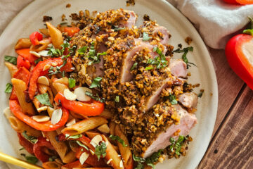 photo culinaire d'un filet mignon en croûte de tomates séchées, amandes et basilic servi avec des pâtes complètes et de poivrons rôtis