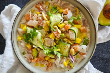 photo culinaire d'un ceviche au lait de coco avec de la mangue, de l'avocat, des chips de coco, du concombre et des rondelles d'oignon rouge