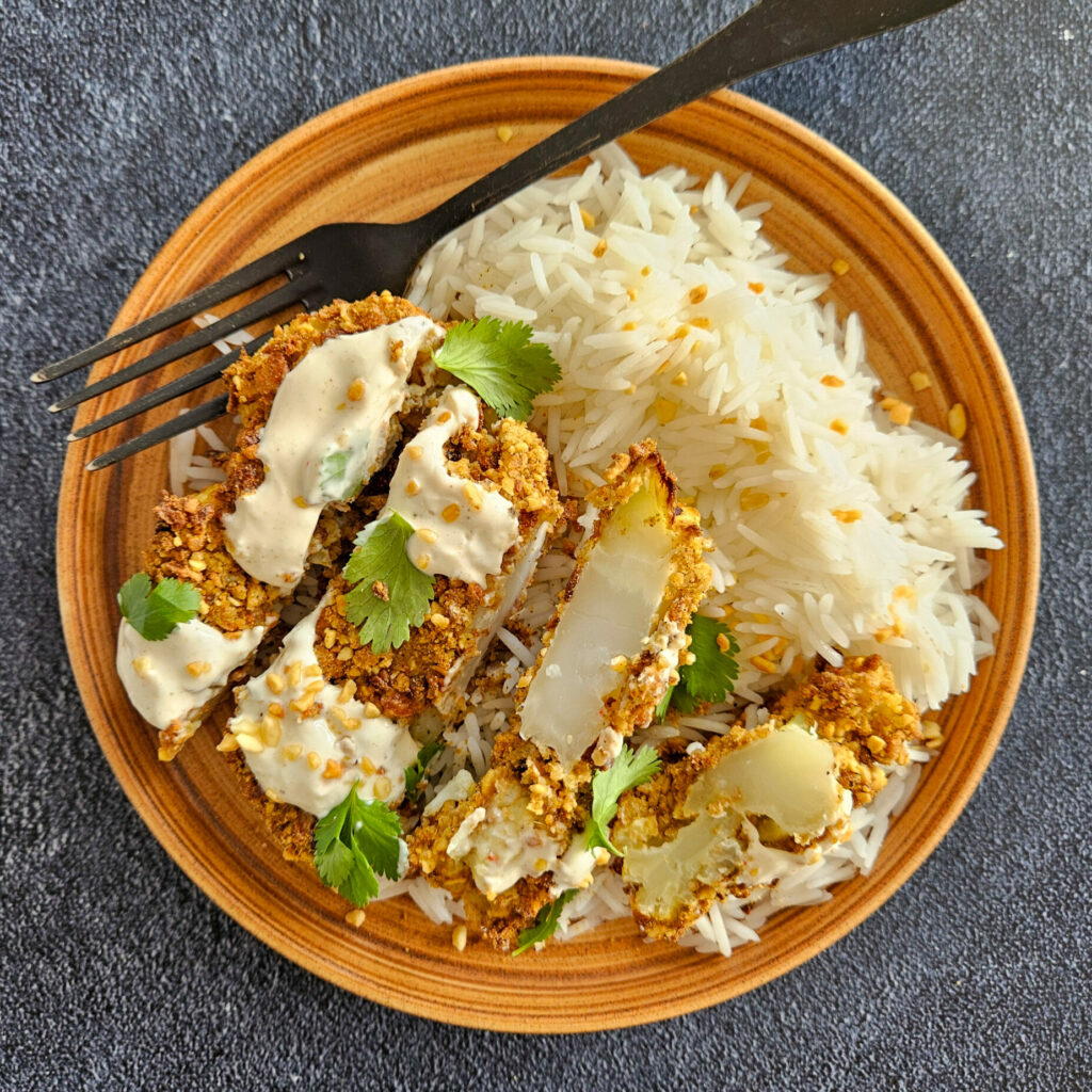 photo culinaire d'un steak de chou-fleur pané aux cacahuètes et épices cajun servi avec du riz basmati et une sauce crémeuse à la purée de cacahuètes