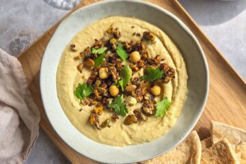 photo culinaire d'un houmous crémeux et granola sucré-salé pistaches et graines avec de la coriandre et servi avec du pain pita
